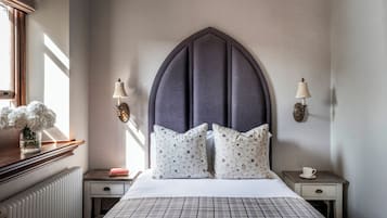 A bedroom with a large bed, two bedside tables, a radiator, a window with curtains, and a wall-mounted lamp.