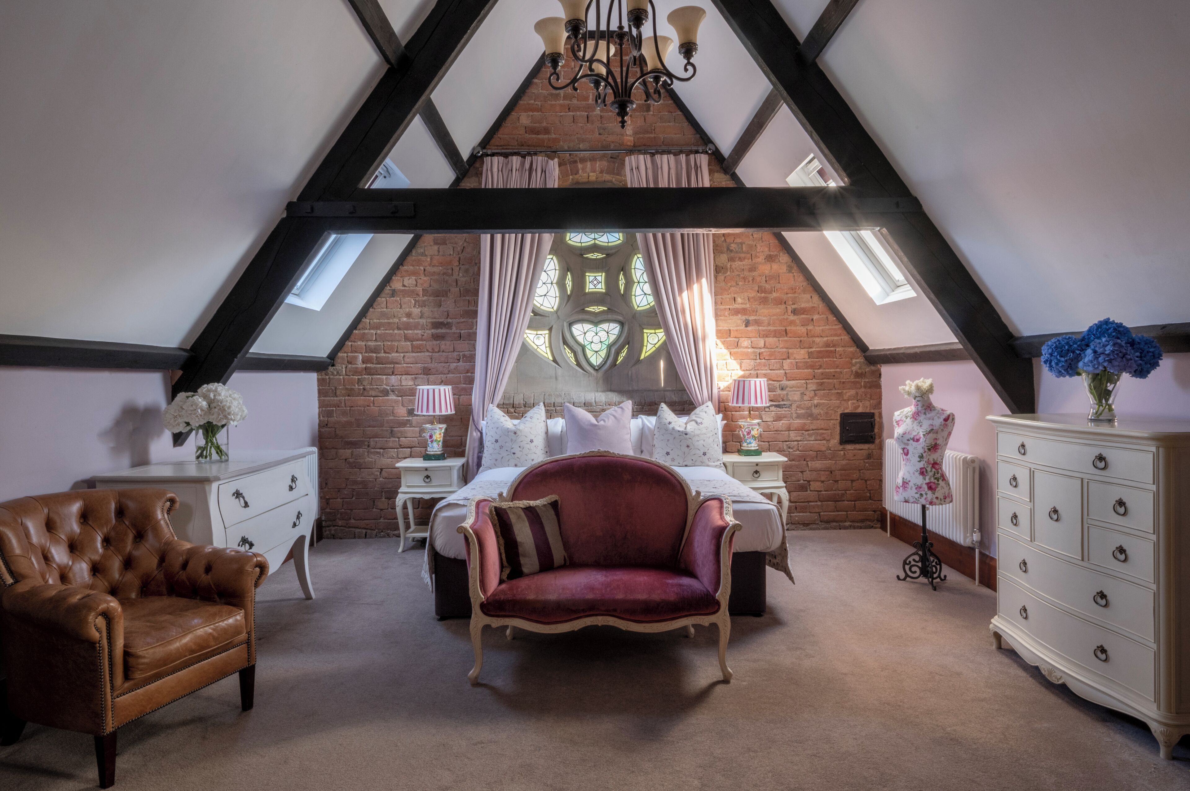 A bedroom with a sloped ceiling, a bed, a red chair, a dresser, and a mannequin.