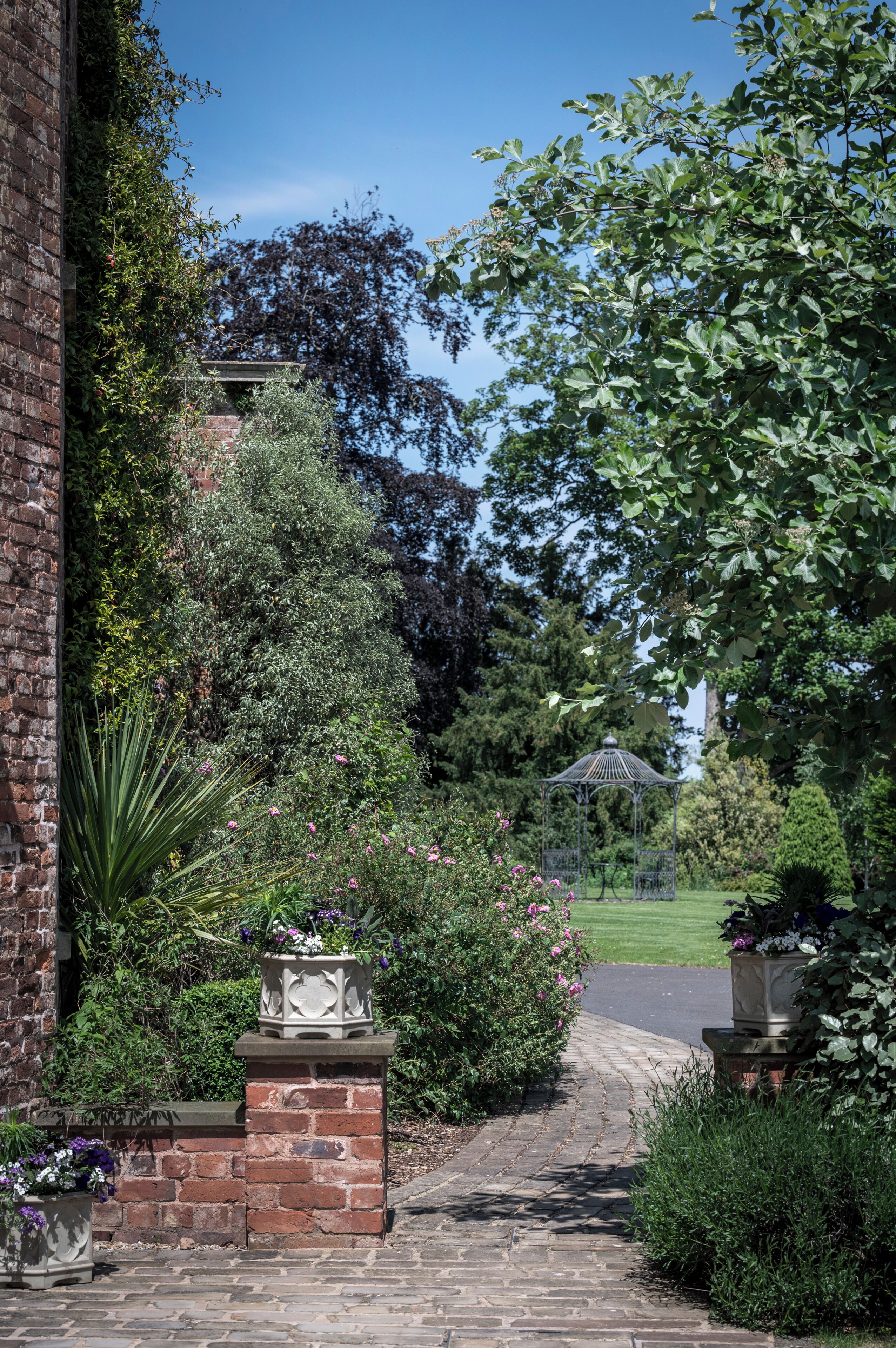 A brick pathway leading to a gazebo in a garden with various plants and flowers.