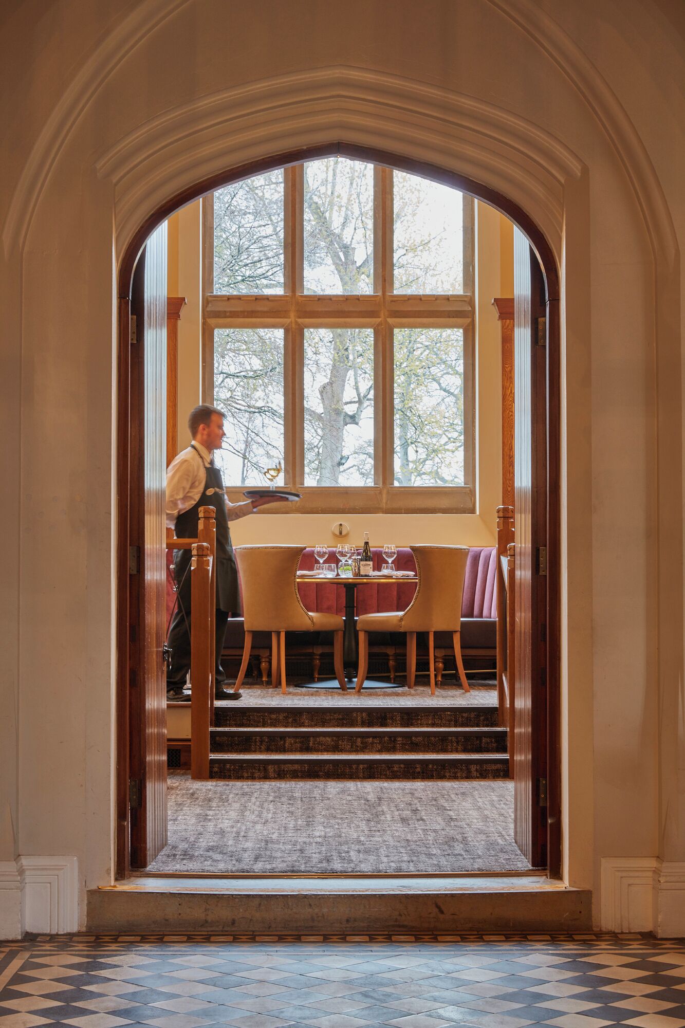A man serving at a table with a view of trees outside a window.