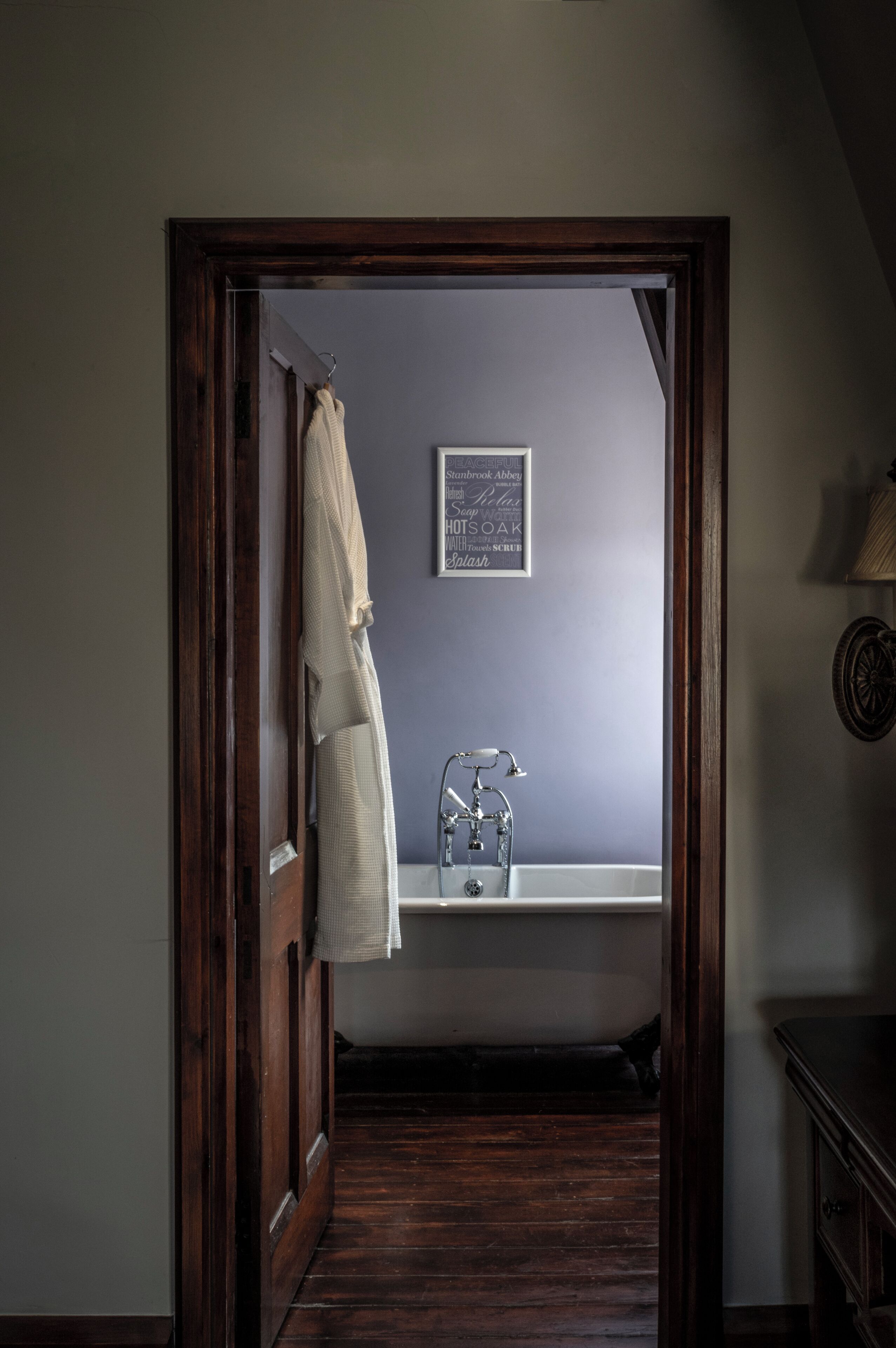 A bathroom with a wooden door, a towel hanging on the door, a sink with a faucet, and a framed word cloud on the wall.