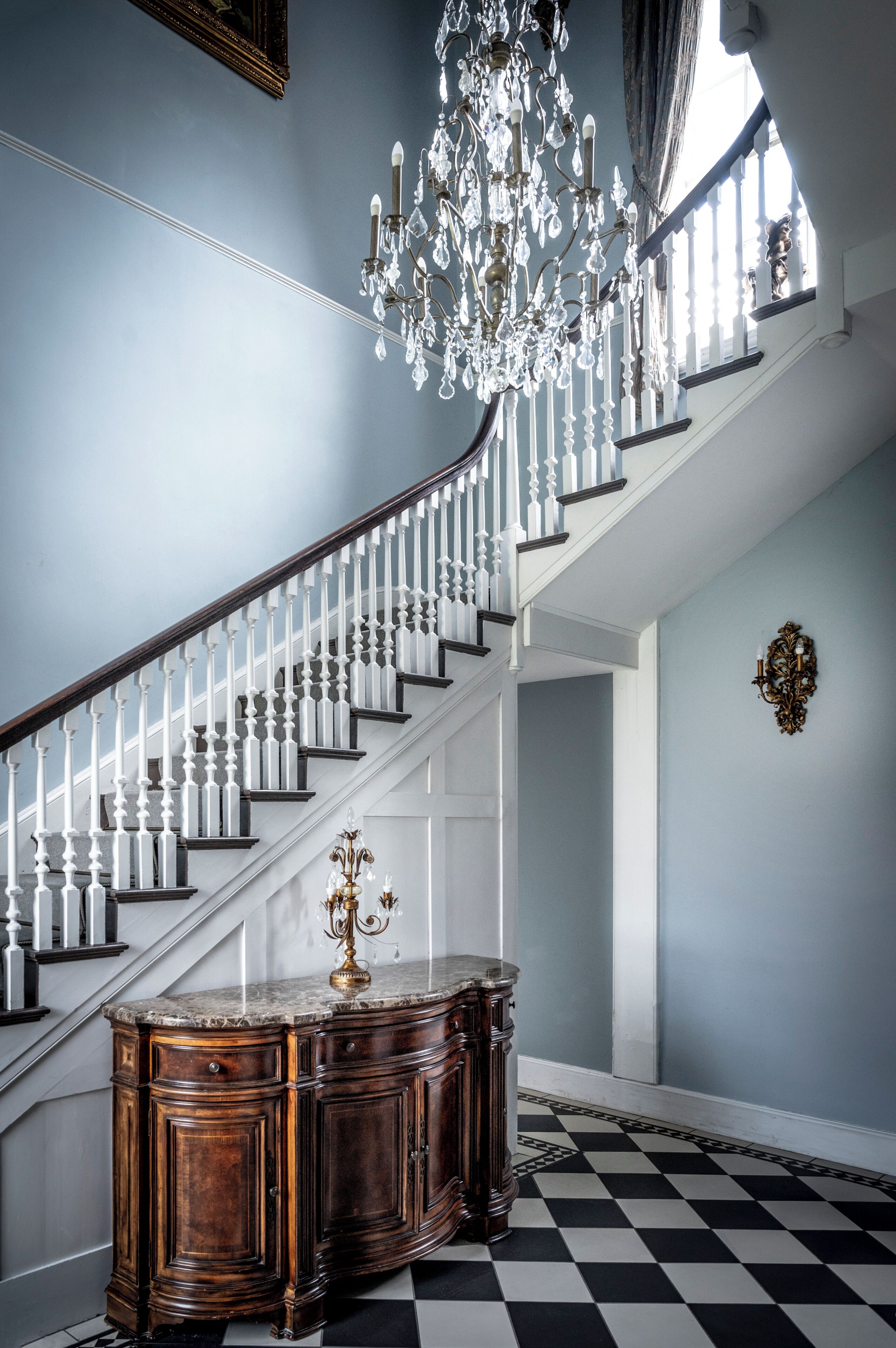 A grand staircase with white balusters, a chandelier, and a marble-top table.