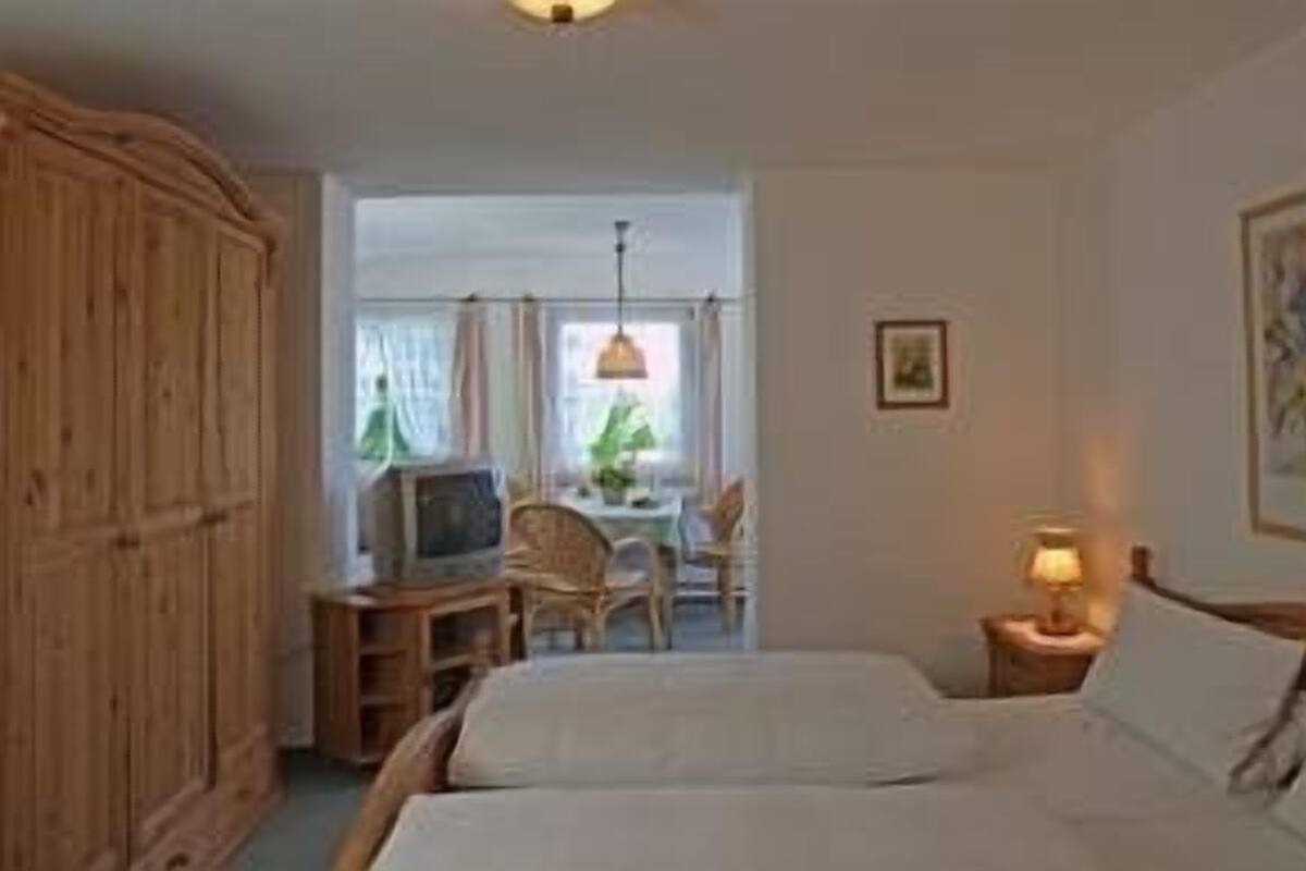 A bedroom with a bed, a desk with a chair, a television, and a lamp.