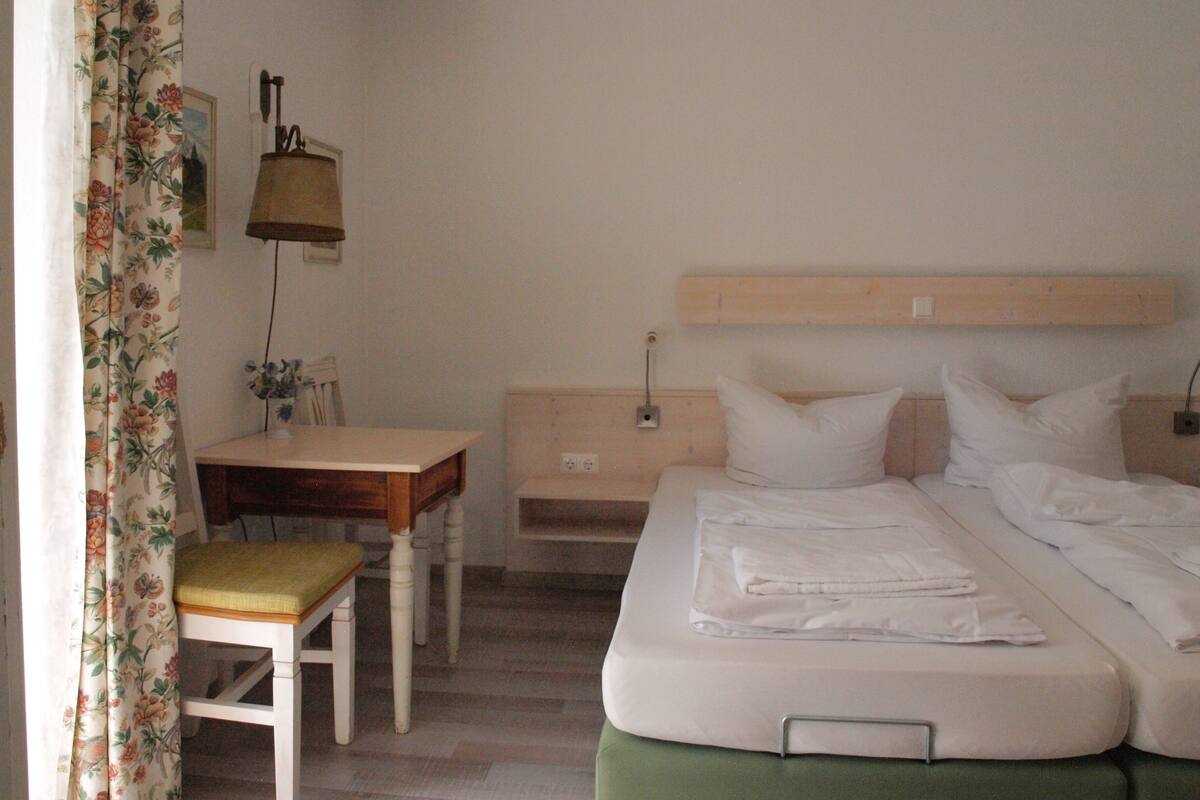 A bedroom with a bed, a bedside table, a chair, and a desk.