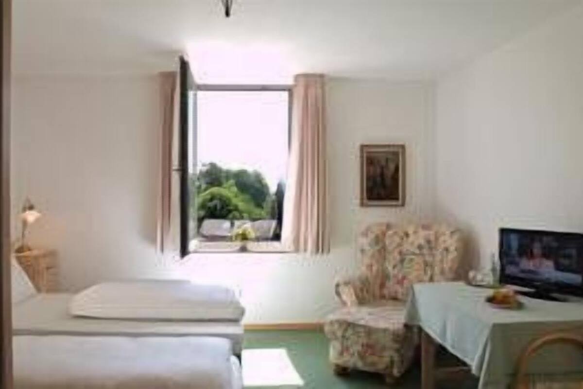 A room with a bed, two armchairs, a television, and a window with curtains.