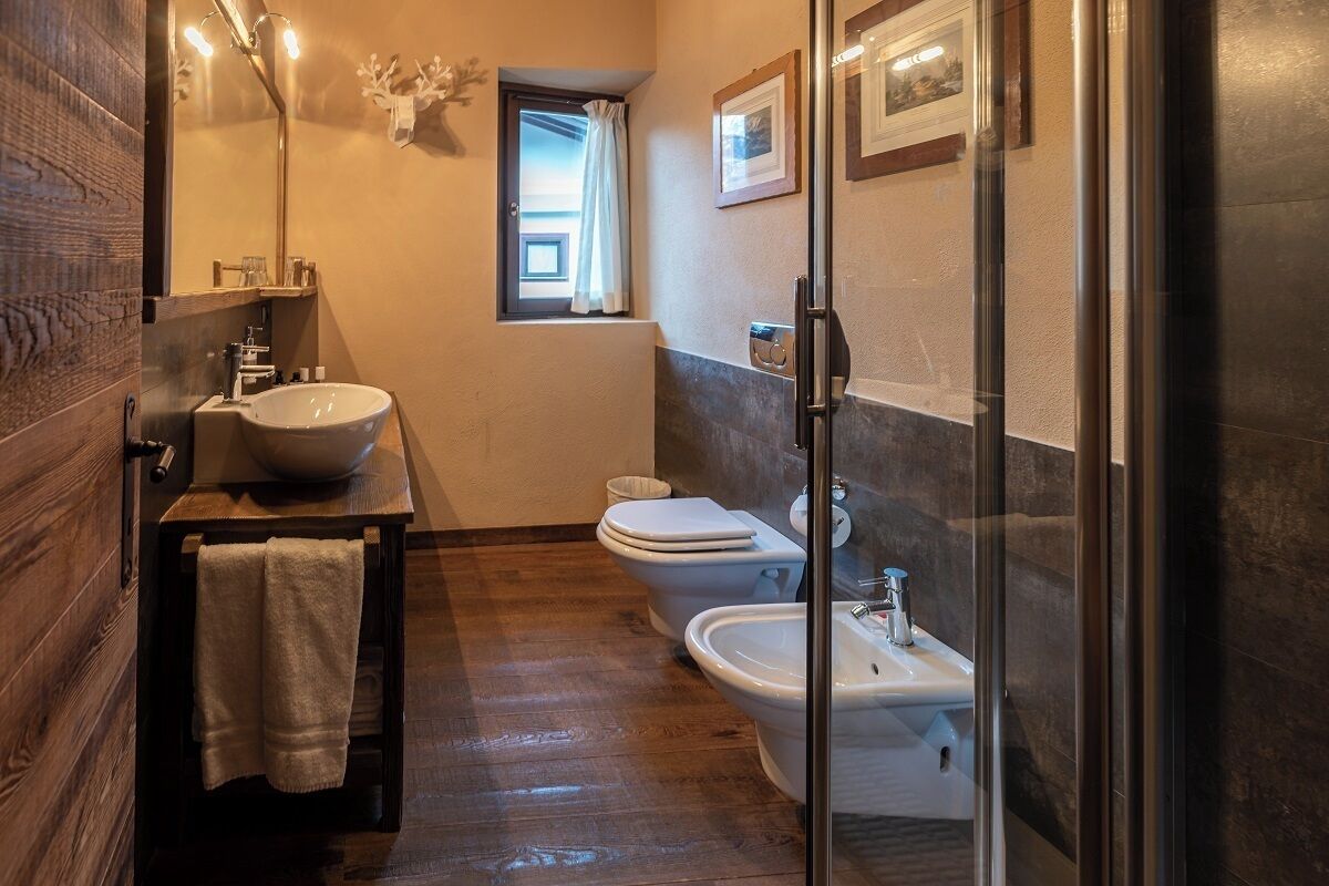 Un baño con tocador de madera, un lavamanos grande, dos inodoros y un bidé.