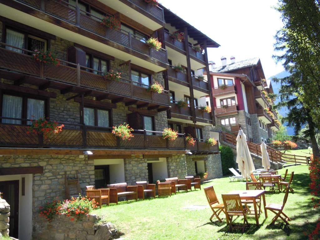 Un hotel de varios pisos con balcones decorados con flores, mobiliario exterior y fachada de piedra.