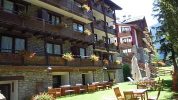 Un hotel de varios pisos con balcones decorados con flores, mobiliario exterior y fachada de piedra.