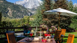 A dining table set outdoors with a mountain view, surrounded by wooden chairs and an umbrella. - Residence Courmaison (Pre-Saint-Didier)