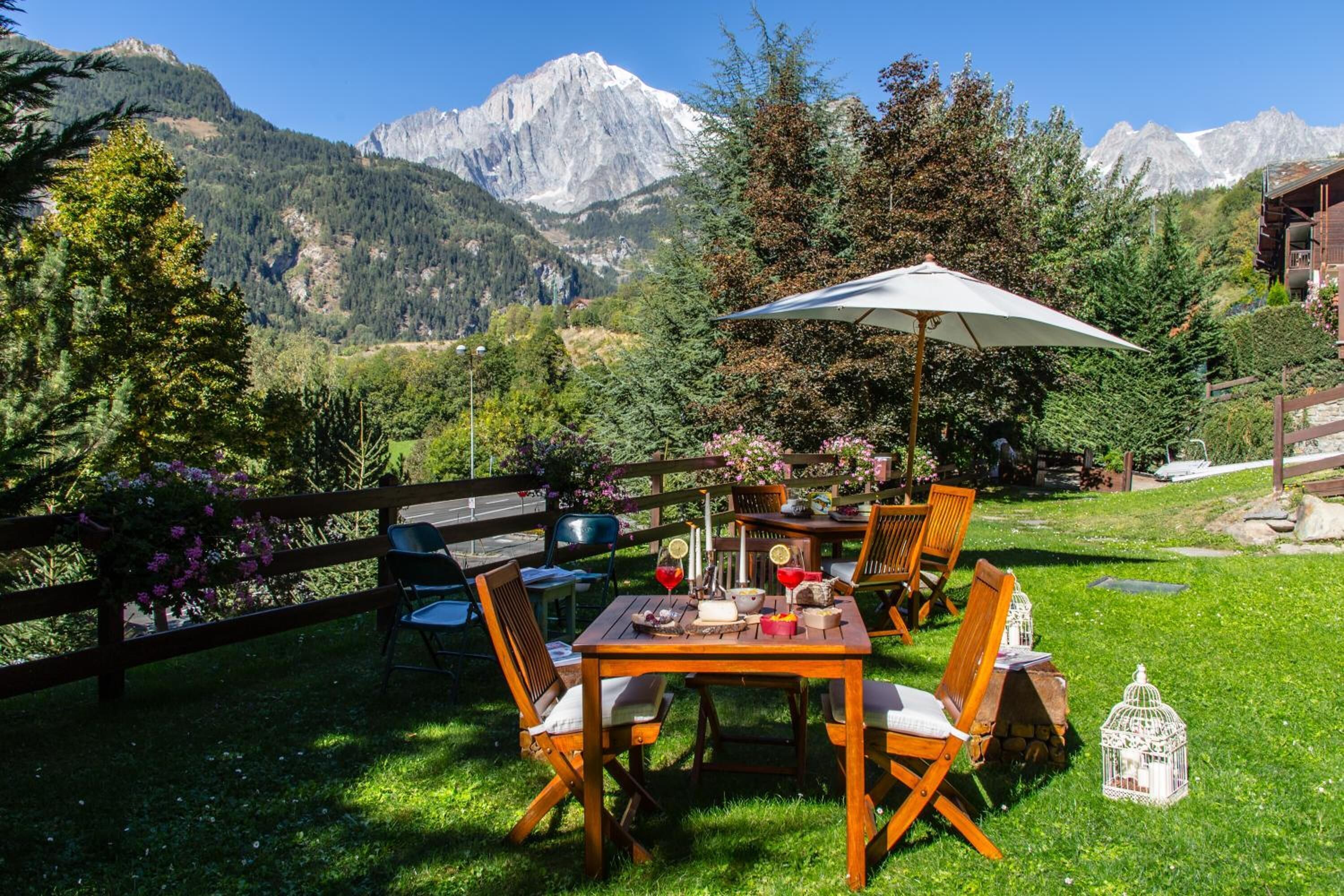 Un área de comedor al aire libre con una mesa y sillas, rodeada por una valla de madera y vistas a montañas.