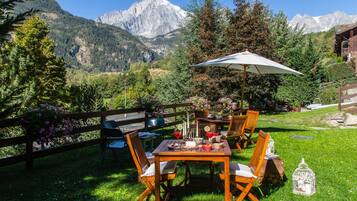 Un área de comedor al aire libre con una mesa y sillas, rodeada por una valla de madera y vistas a montañas.