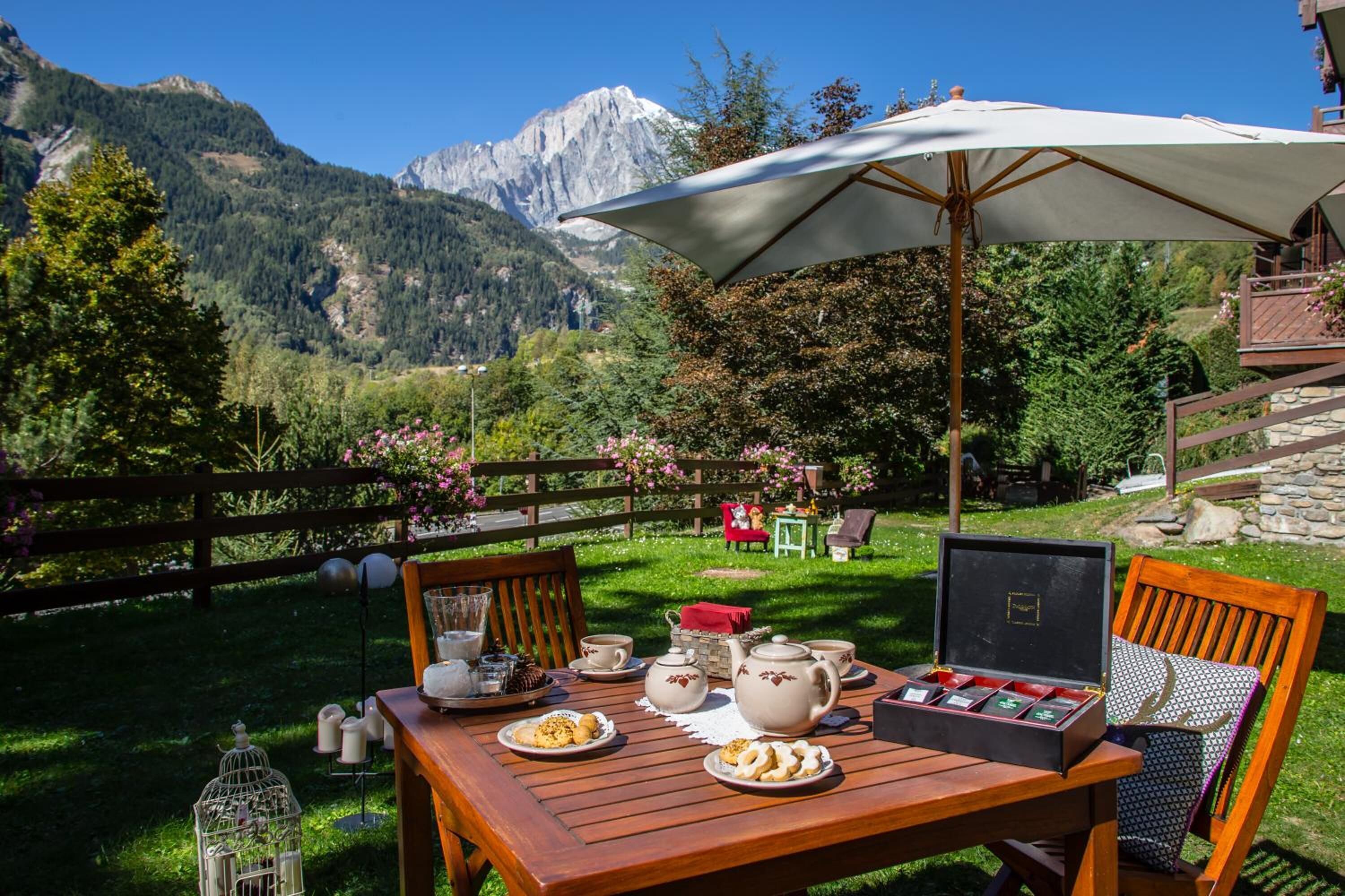 Un área de comedor al aire libre con una mesa dispuesta para el té, rodeada por un cerco de madera y una vista de montaña al fondo.