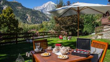 Un área de comedor al aire libre con una mesa dispuesta para el té, rodeada por un cerco de madera y una vista de montaña al fondo.