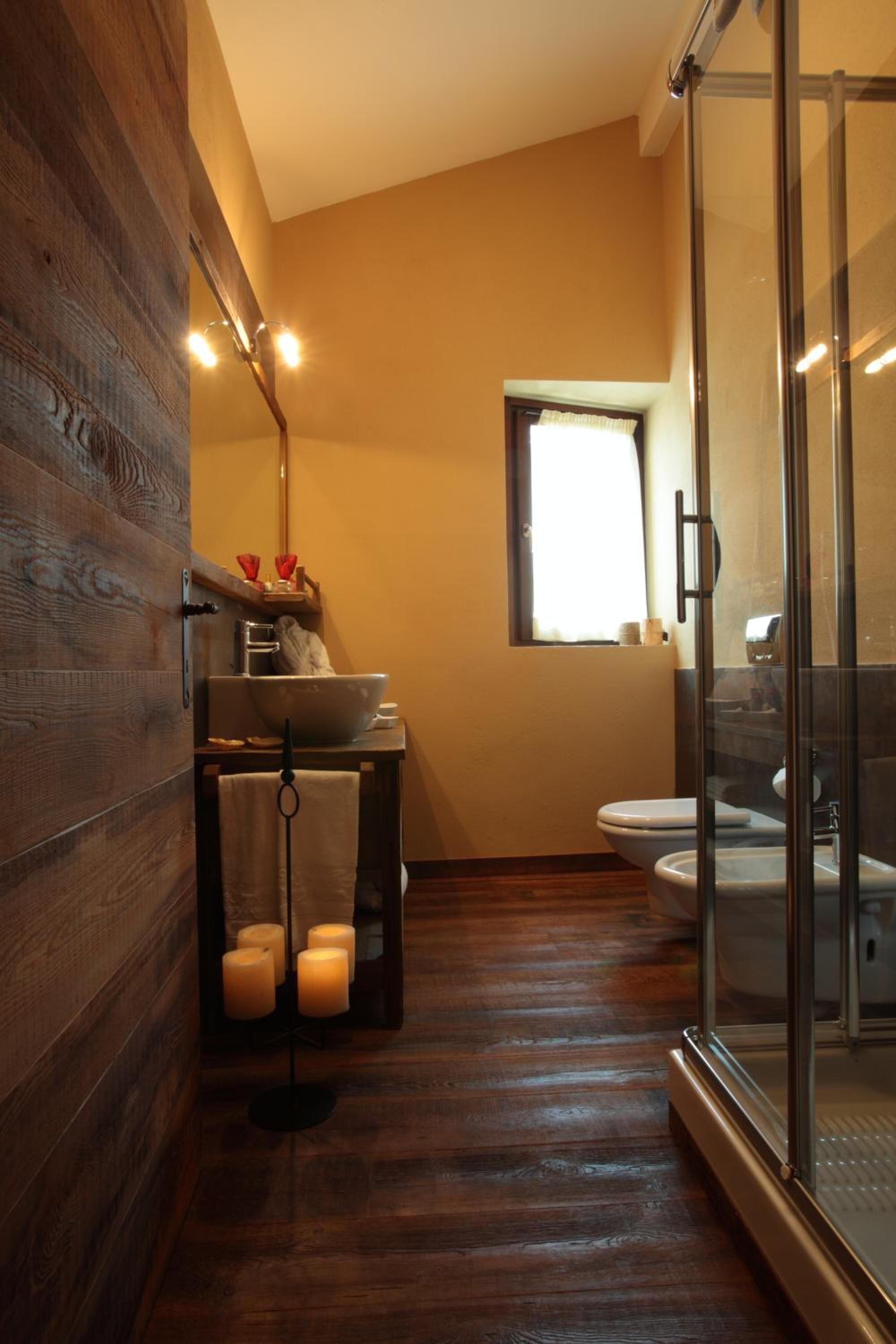 Un baño moderno con suelo de madera, cabina de ducha de vidrio, lavamanos con espejo e inodoro.