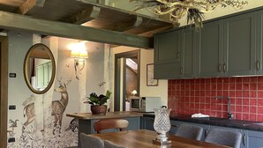 A dining area with a wooden table and chairs, a chandelier, and a kitchen with red tiles and cabinets. - Residence Courmaison (Pre-Saint-Didier)
