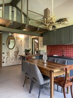 Un comedor con mesa y sillas de madera, un candelabro, y una cocina con baldosas y armarios rojos.
