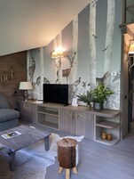 Una sala de estar moderna con un televisor de pantalla plana, armarios de madera, un sofá gris, una mesa de centro y una pared decorativa con papel tapiz de temática natural.