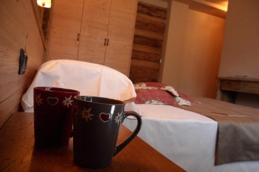 Un interior de madera con una cama, una mesita de noche y dos tazas sobre una mesa.