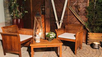 A wooden outdoor seating area with two chairs and a table, a lantern, and a potted plant.