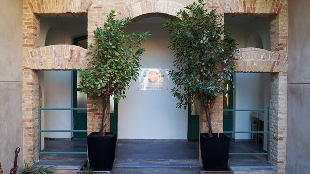 Une entrée avec une arche en pierre, deux plantes en pot et un panneau sur le mur.