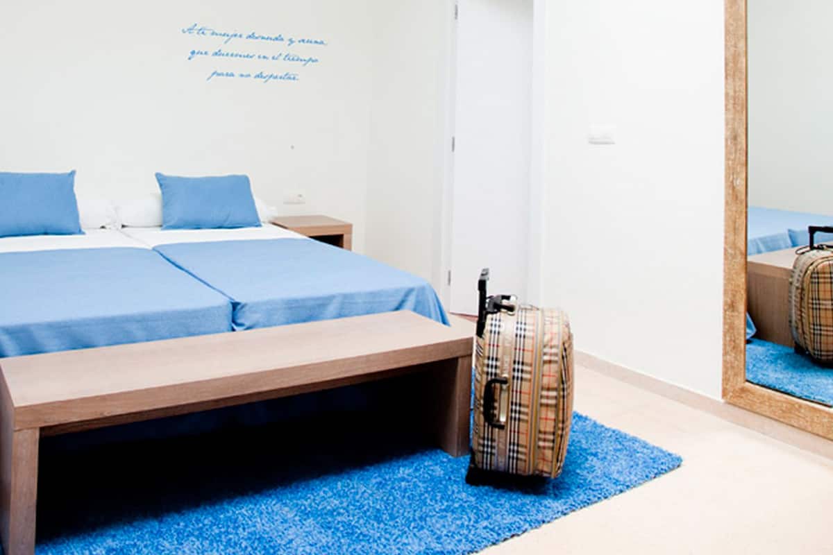 Una habitación de hotel con cama, banca, maleta y espejo.