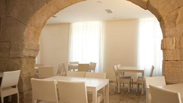A dining area with stone arches, white wicker furniture, and large windows.