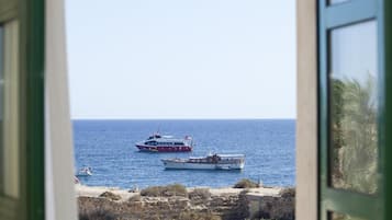 Vista del mar con dos barcos, uno más grande y otro más pequeño, desde una ventana con vista a una costa rocosa.