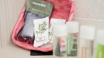 Un baño con una cesta de mimbre rosa que contiene una bolsa verde con la etiqueta 'r.nomenitii' y una bolsita blanca con la etiqueta 'JASON SOFT'. También hay varias botellas pequeñas con tapas blancas, probablemente conteniendo productos de baño.