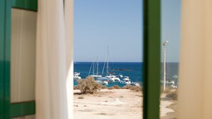 Une vue sur une marina où sont amarrés plusieurs voiliers, une plage de sable et un ciel bleu dégagé.