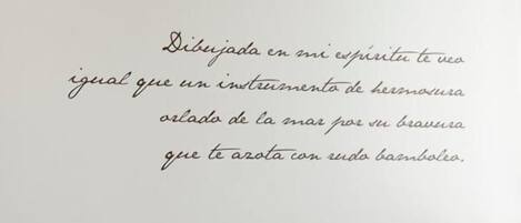 Une chambre à coucher avec un lit, des oreillers et un mur orné d’une citation en espagnol.