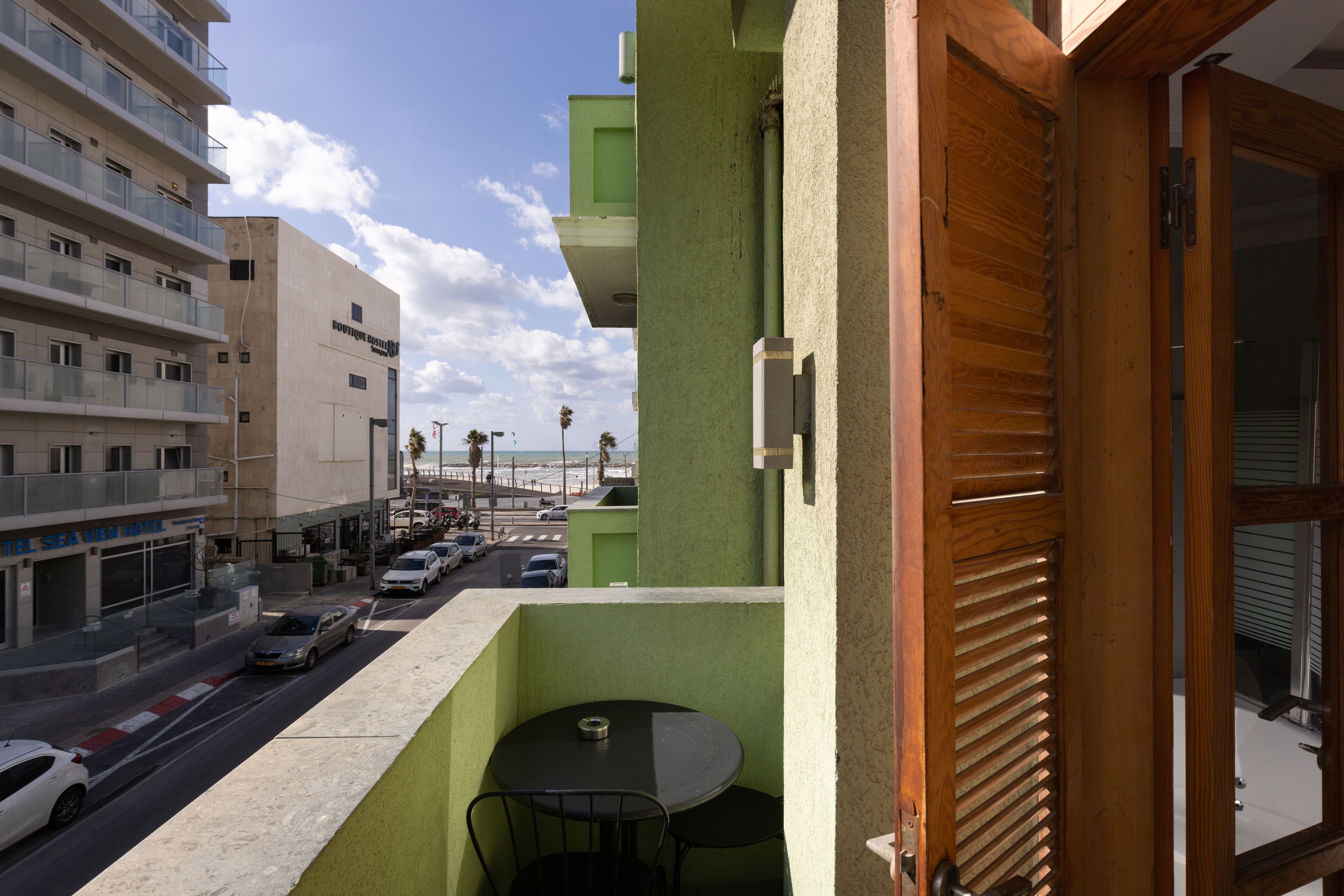 Un balcon avec une table et des chaises, donnant sur une rue bordée de voitures garées et sur un hôtel en arrière-plan.