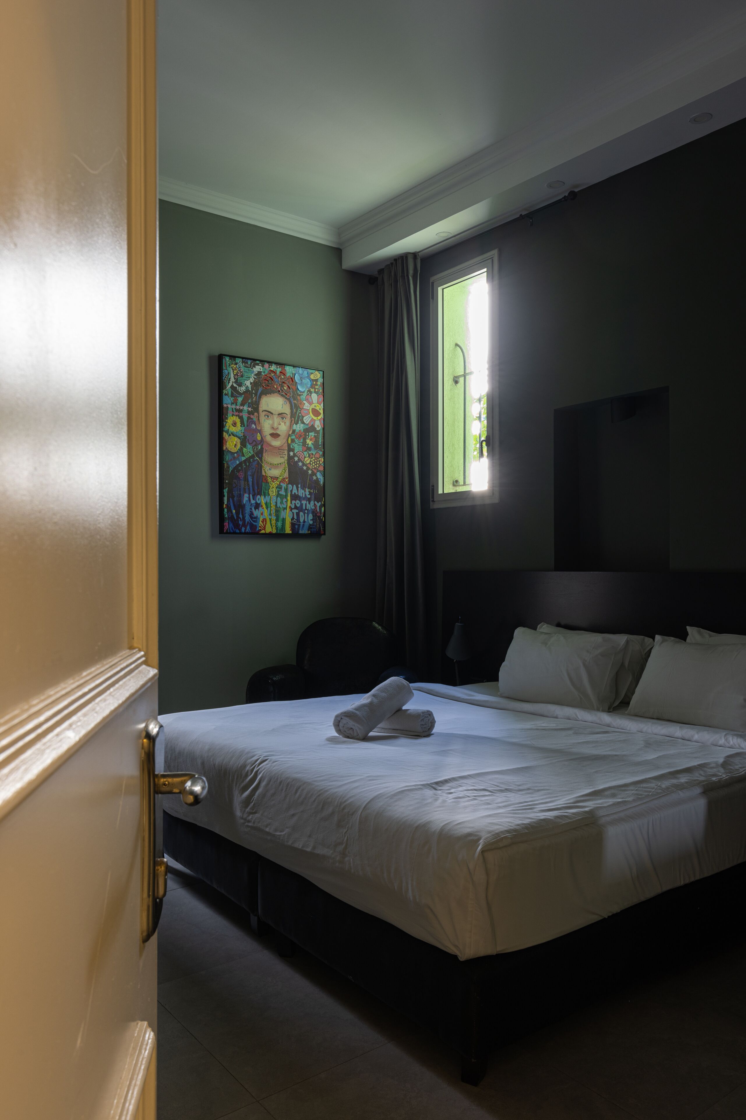 Una habitación de hotel con cama, un cuadro en la pared, una ventana con cortinas y un televisor también en la pared.