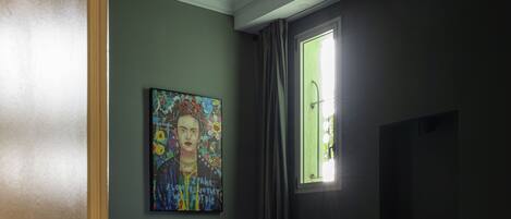 A hotel room with a bed, a painting on the wall, a window with curtains, and a television on the wall.