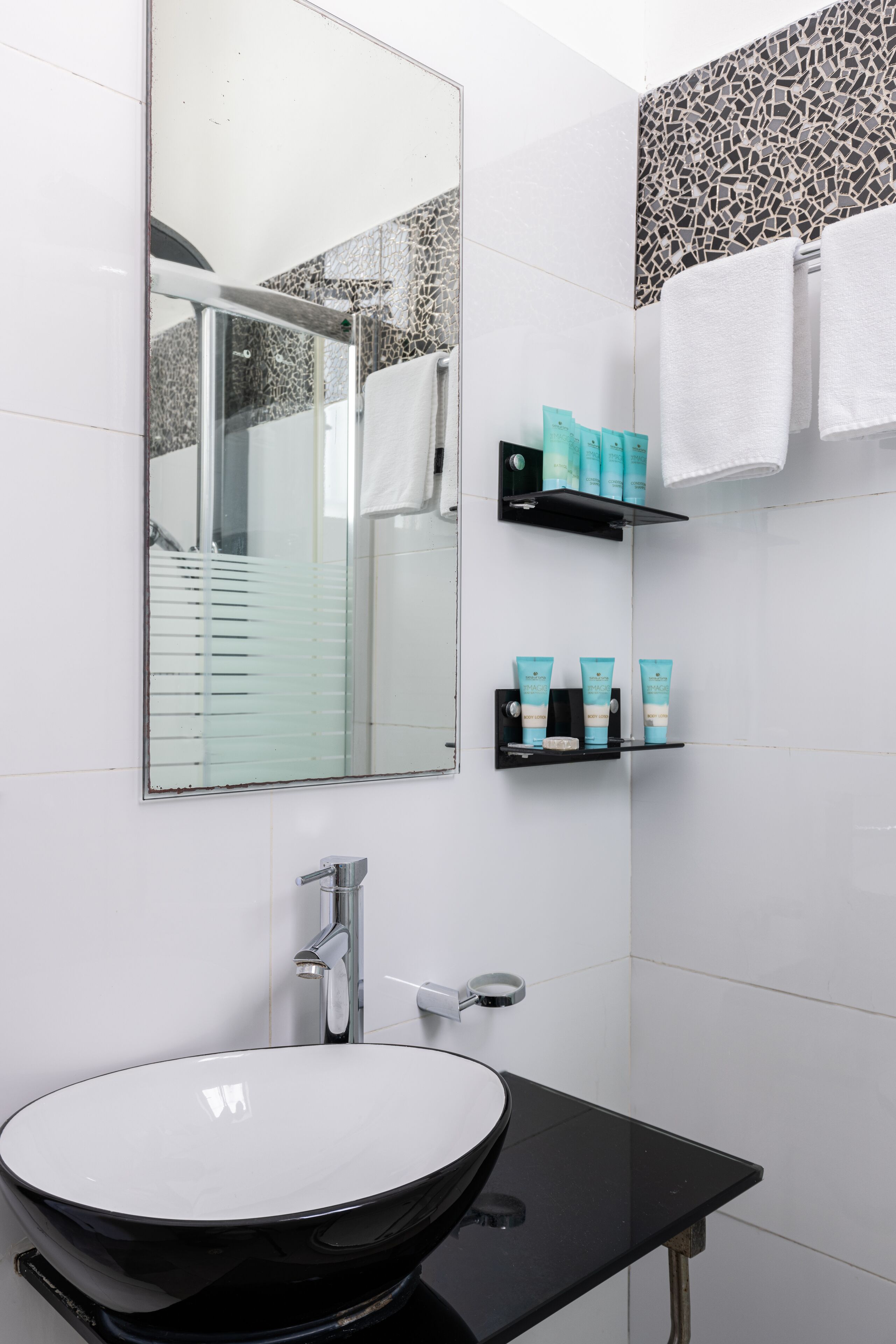 Une salle de bain moderne avec un grand miroir, un lavabo noir et des étagères remplies de produits de toilette.