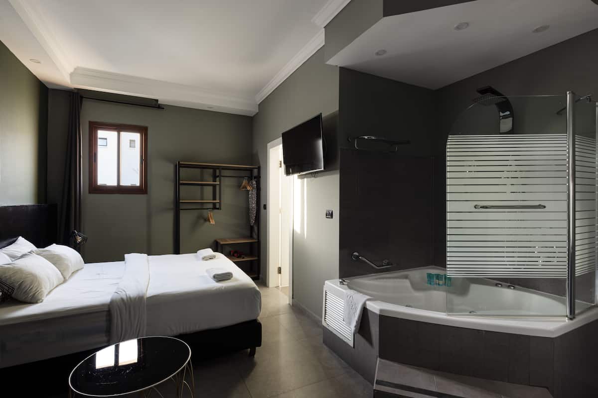 Una habitación de hotel moderna con cama, una mesita, televisión, ducha y bañera.