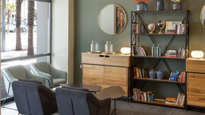 Un interior moderno con zona de estar, estanterías y un amplio ventanal con vistas a palmeras.