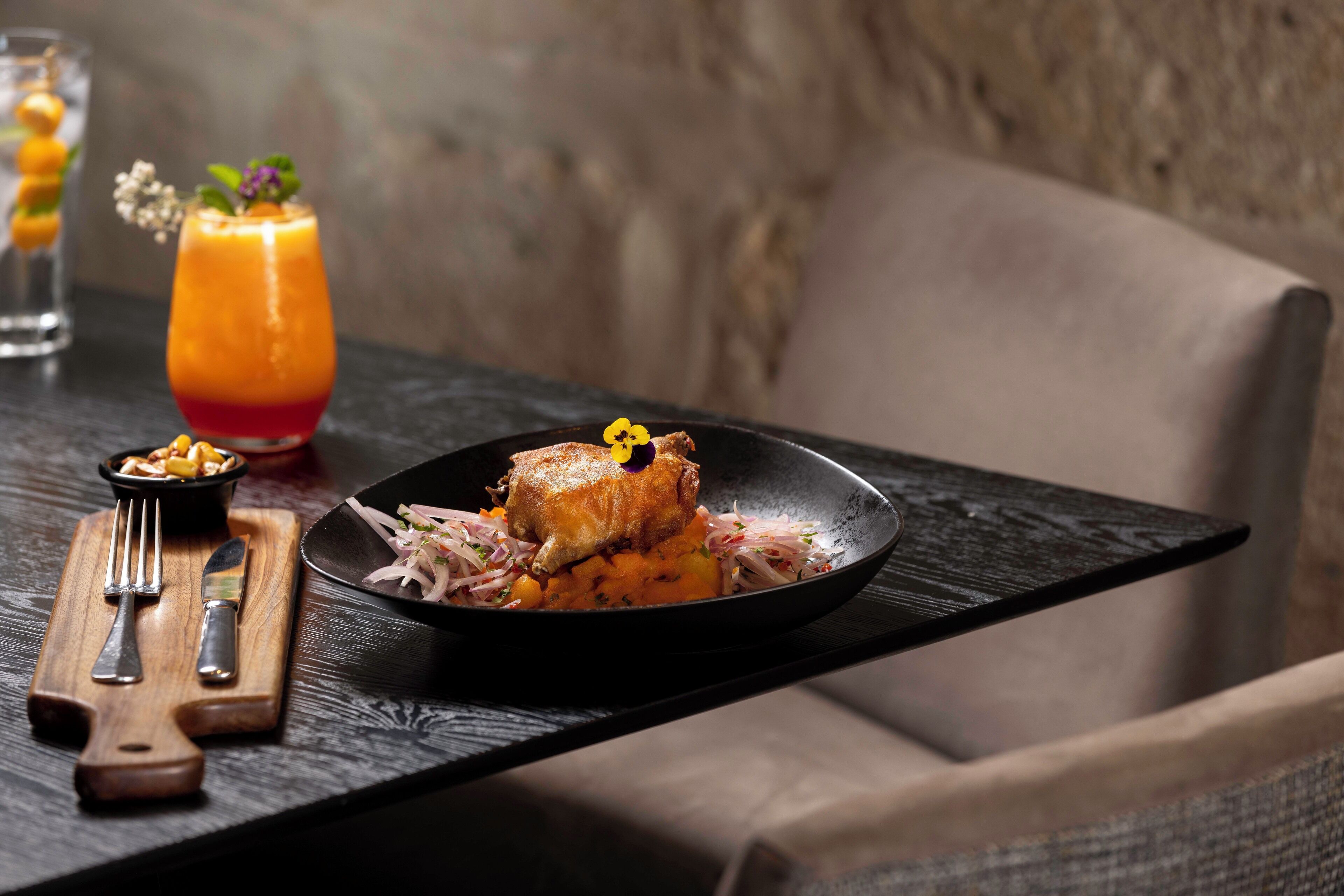 A dining table with a black plate of food, a fork, knife, and a glass of drink.