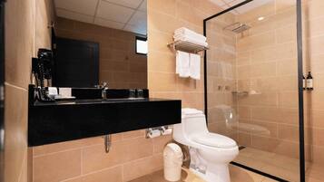 Un baño moderno con encimera negra, inodoro, ducha envuelta en vidrio y paredes con azulejos color beige.