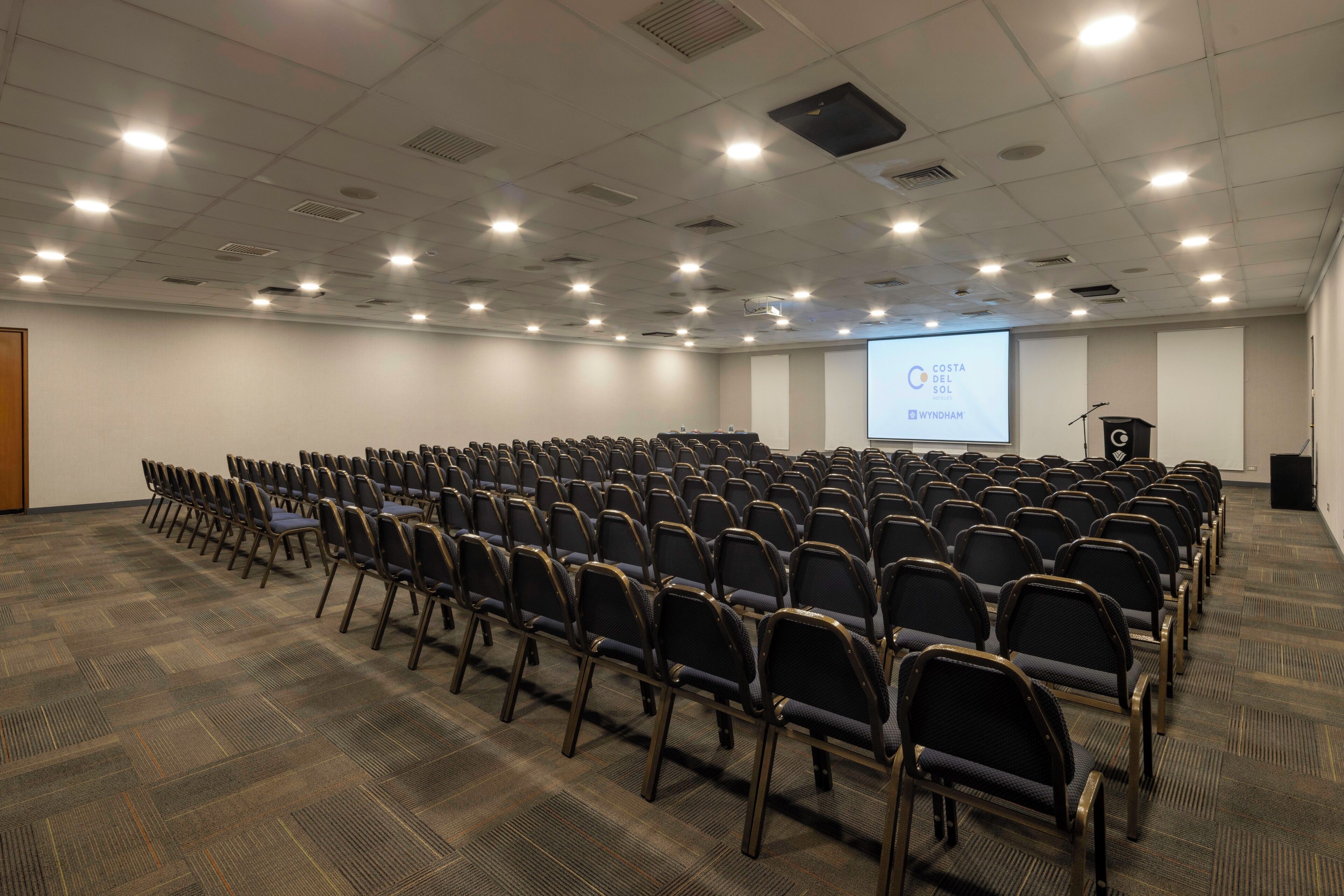 A conference room with rows of chairs, a projector screen, and a podium.