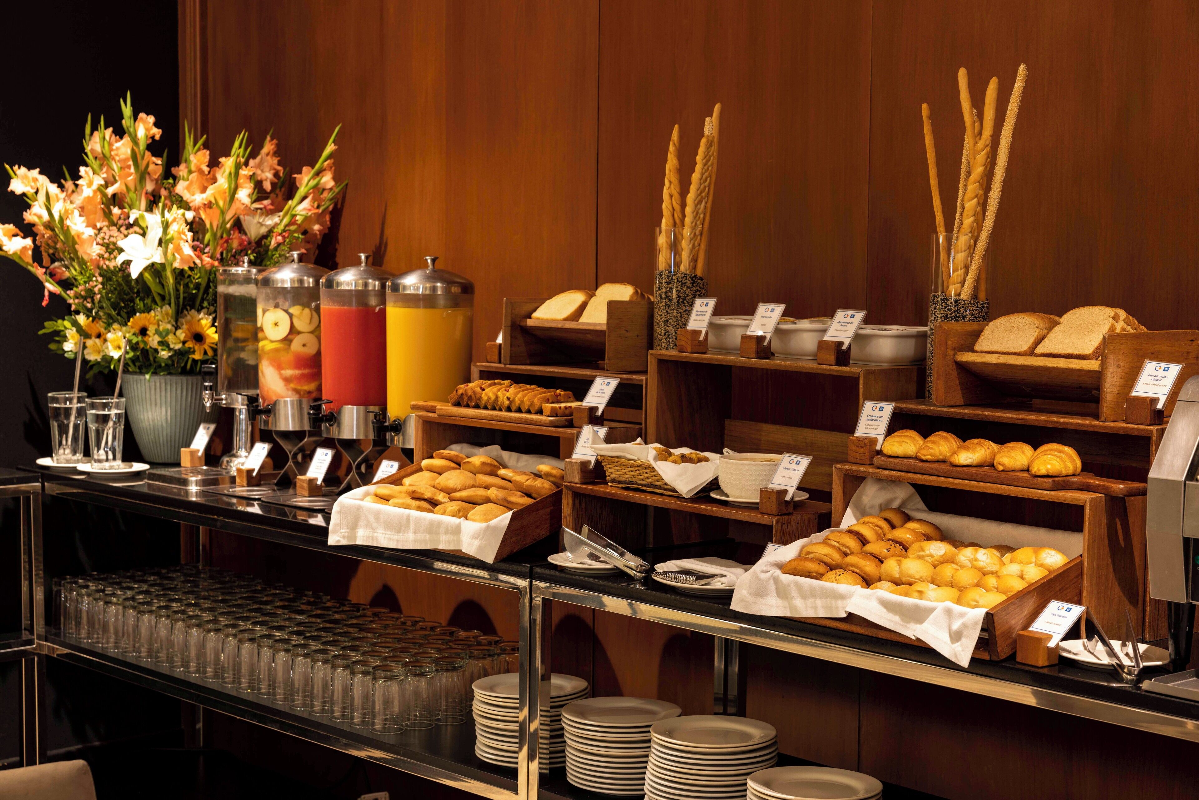 A buffet with various food items and beverages, including bread, pastries, and a fruit display.
