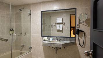 A bathroom with a glass-enclosed shower, a sink with a mirror, and a telephone.