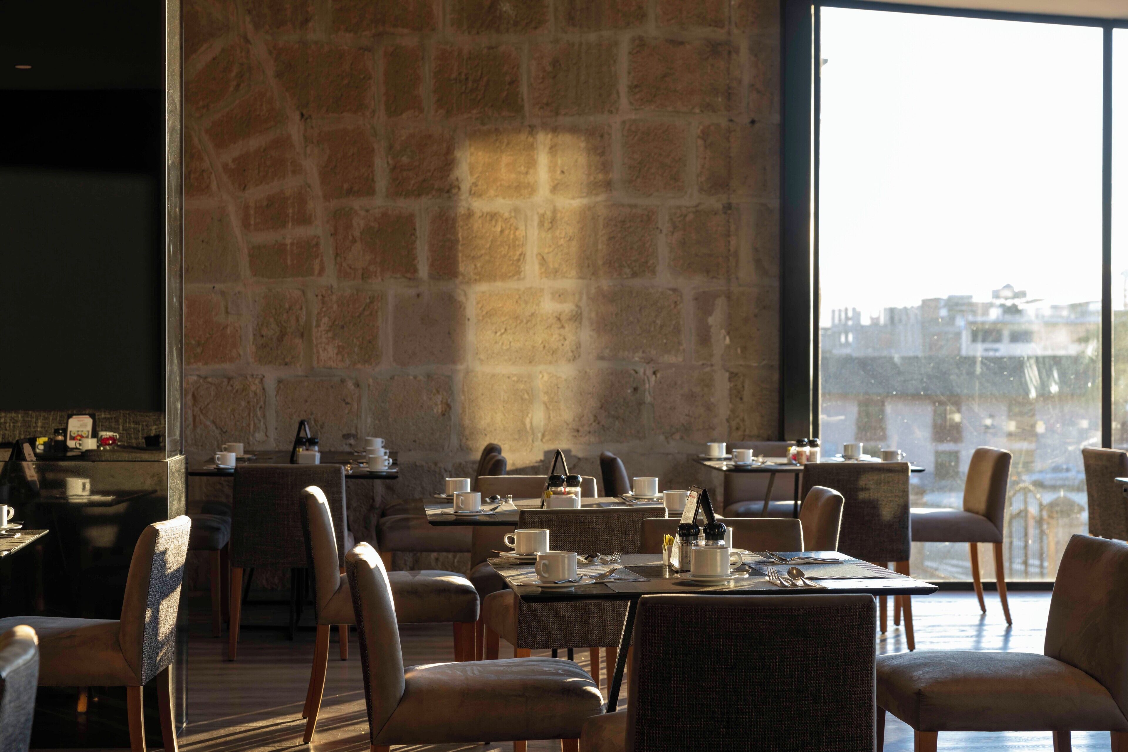 A restaurant with tables set for dining, chairs, and a stone wall.