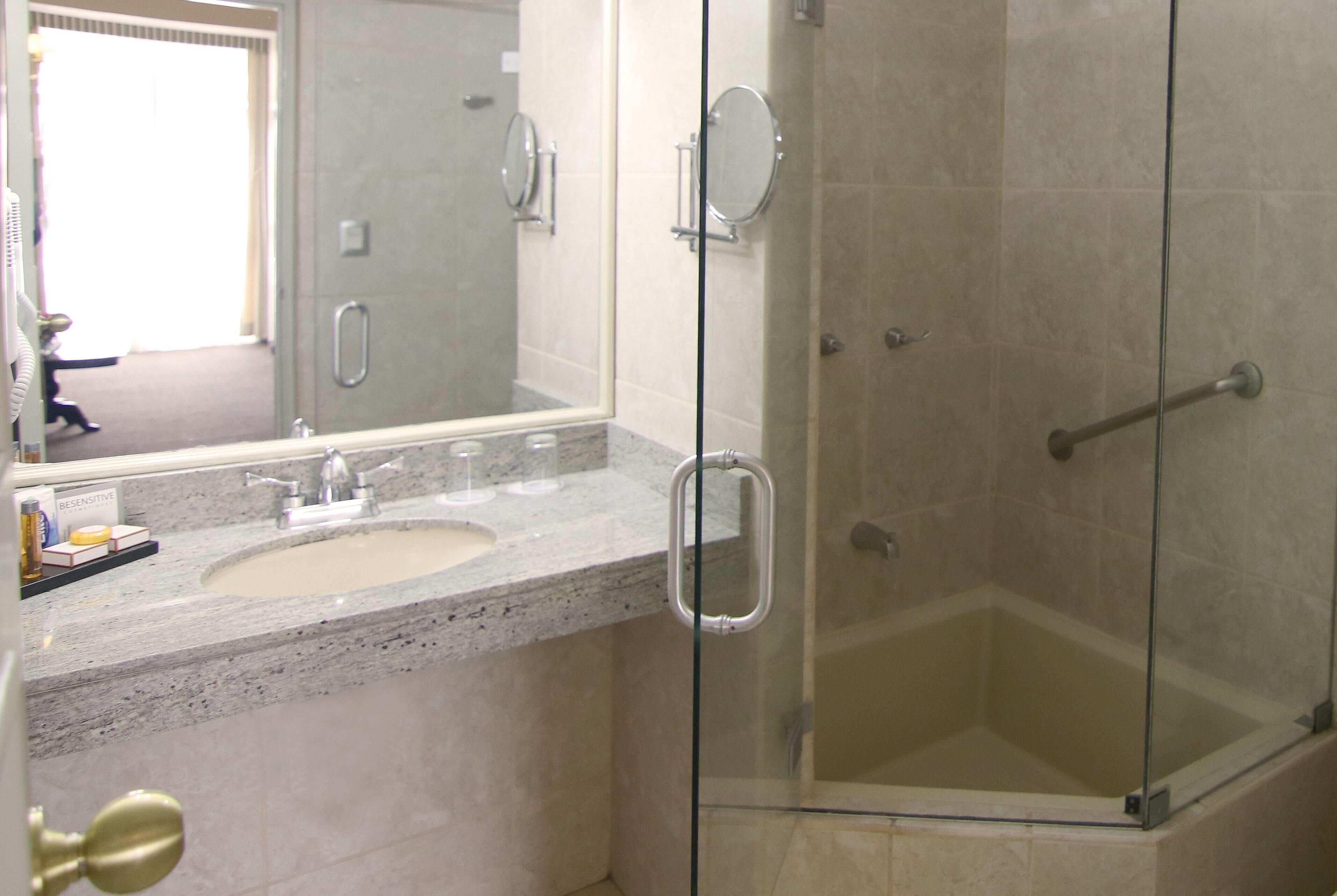 A bathroom with a glass-enclosed shower, a sink with a marble countertop, and a mirror.