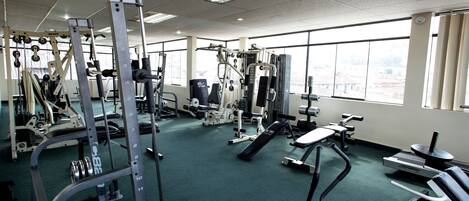 A gym with various exercise equipment, large windows, and a green carpet.