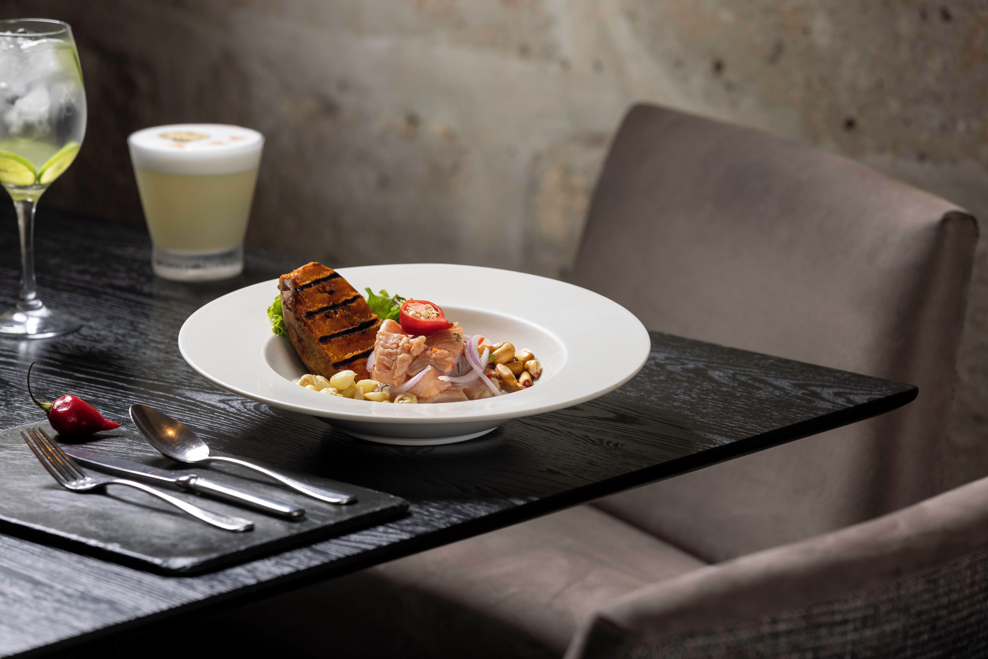 Prato de frango grelhado com legumes sobre mesa escura, acompanhado por um copo de bebida branca e um pimentão vermelho.