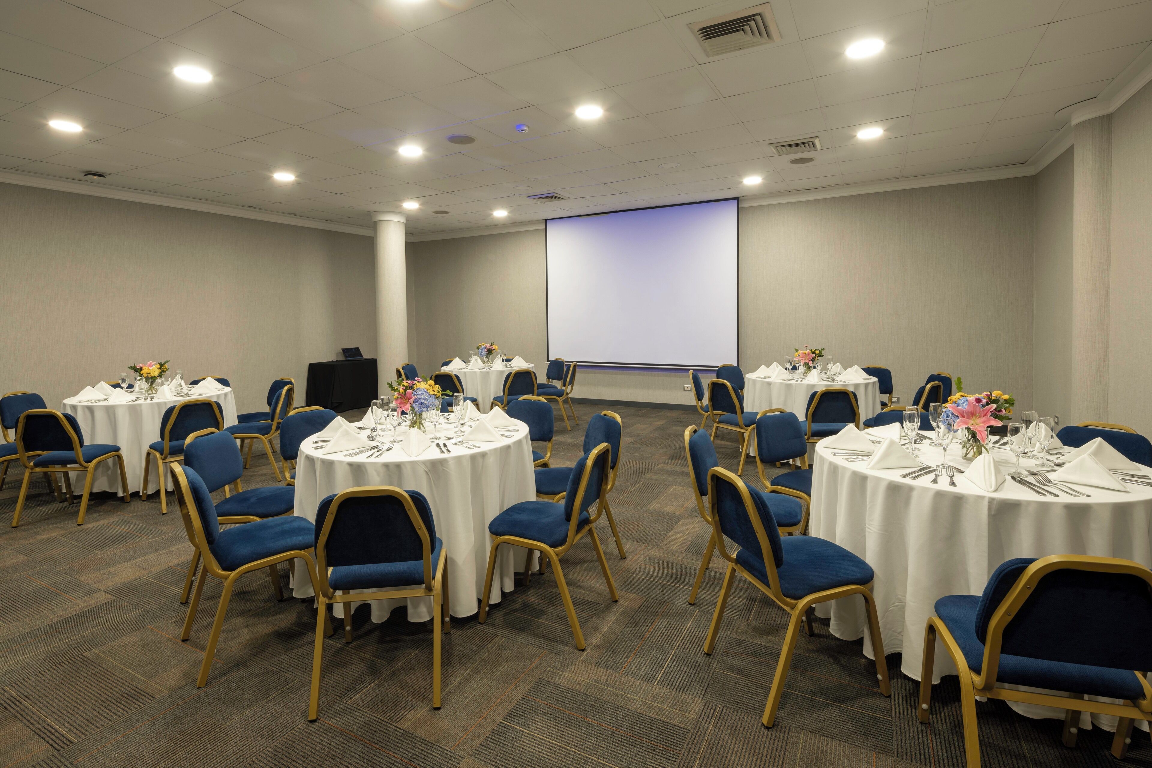 A conference room with round tables, blue chairs, and white tablecloths.