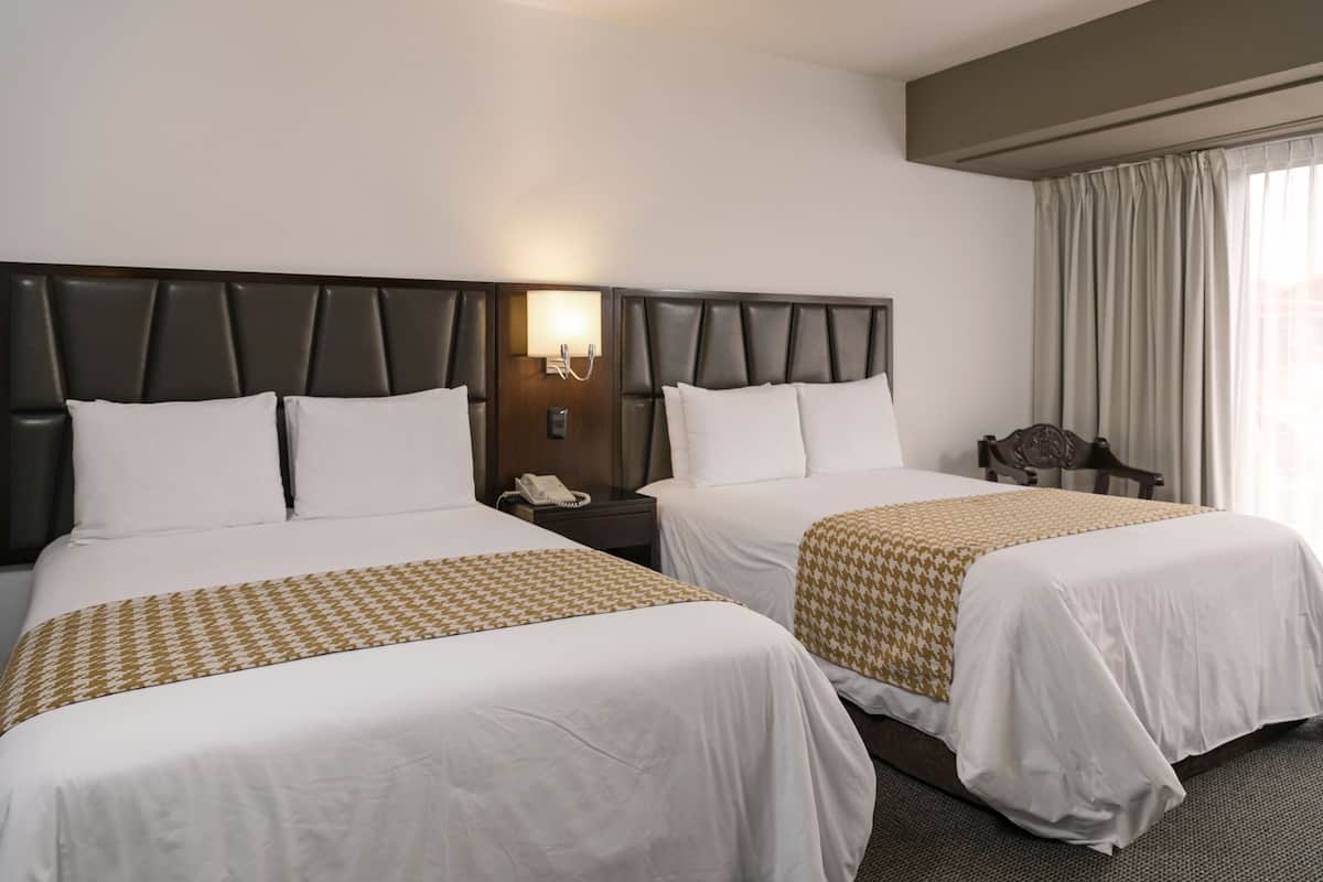 A hotel room with two beds, a nightstand with a phone, and a chair.