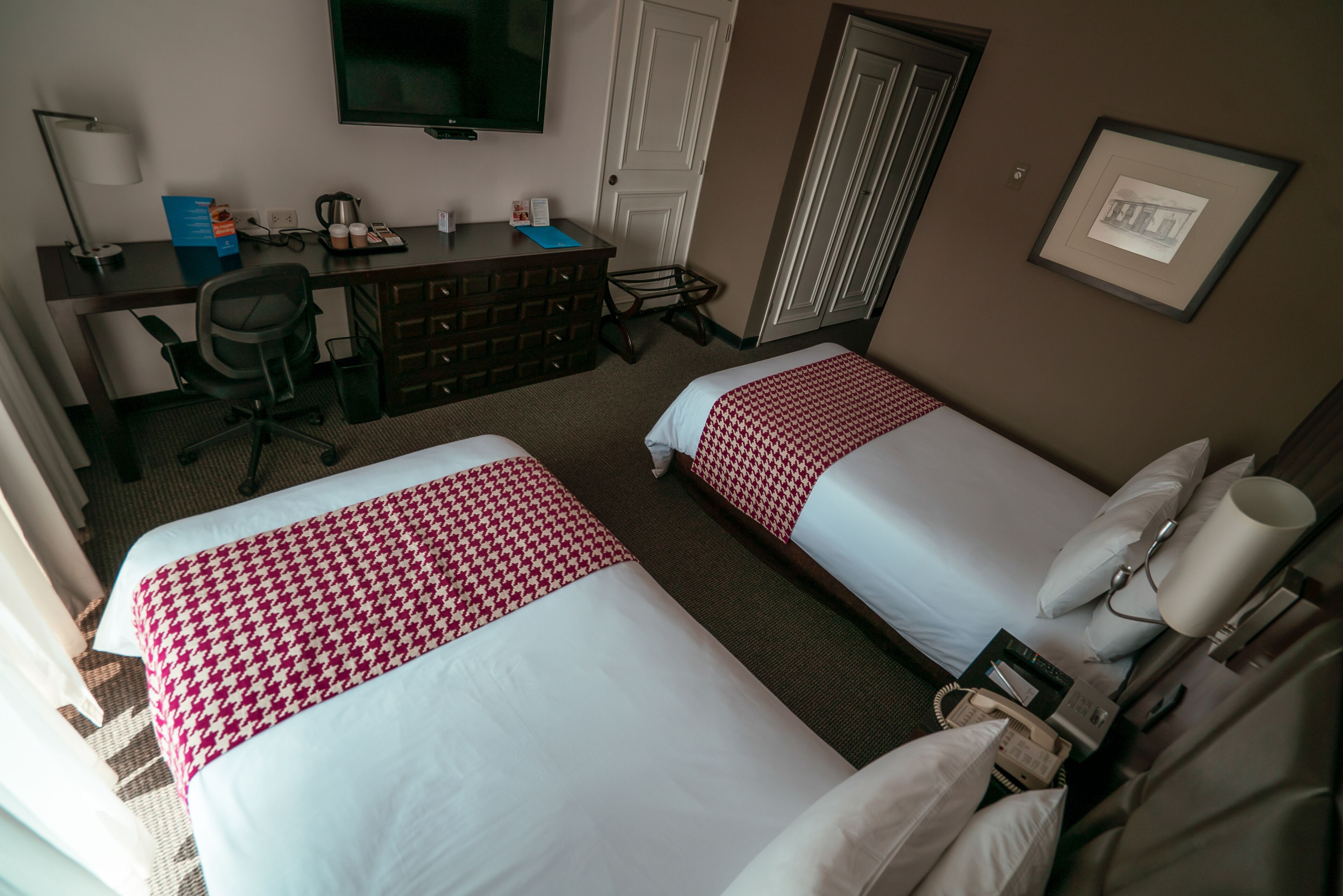A hotel room with two beds, a desk with a chair, a television, a coffee maker, and a framed picture on the wall.