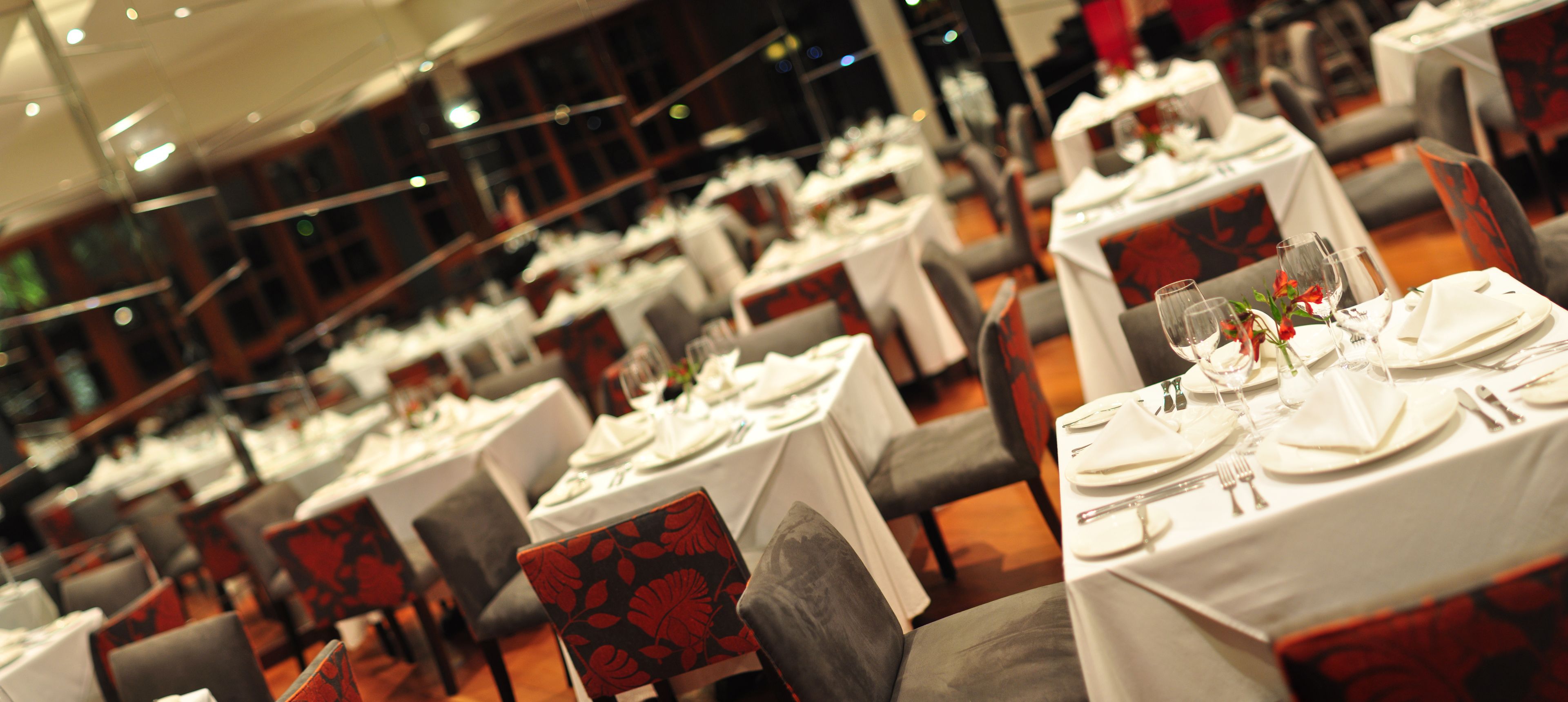 Un restaurante con varias mesas preparadas para comer, cada una con manteles blancos y cubiertos ordenados.