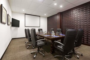 A conference room with a long table, black chairs, a projector screen, and a decorative wooden panel wall.
